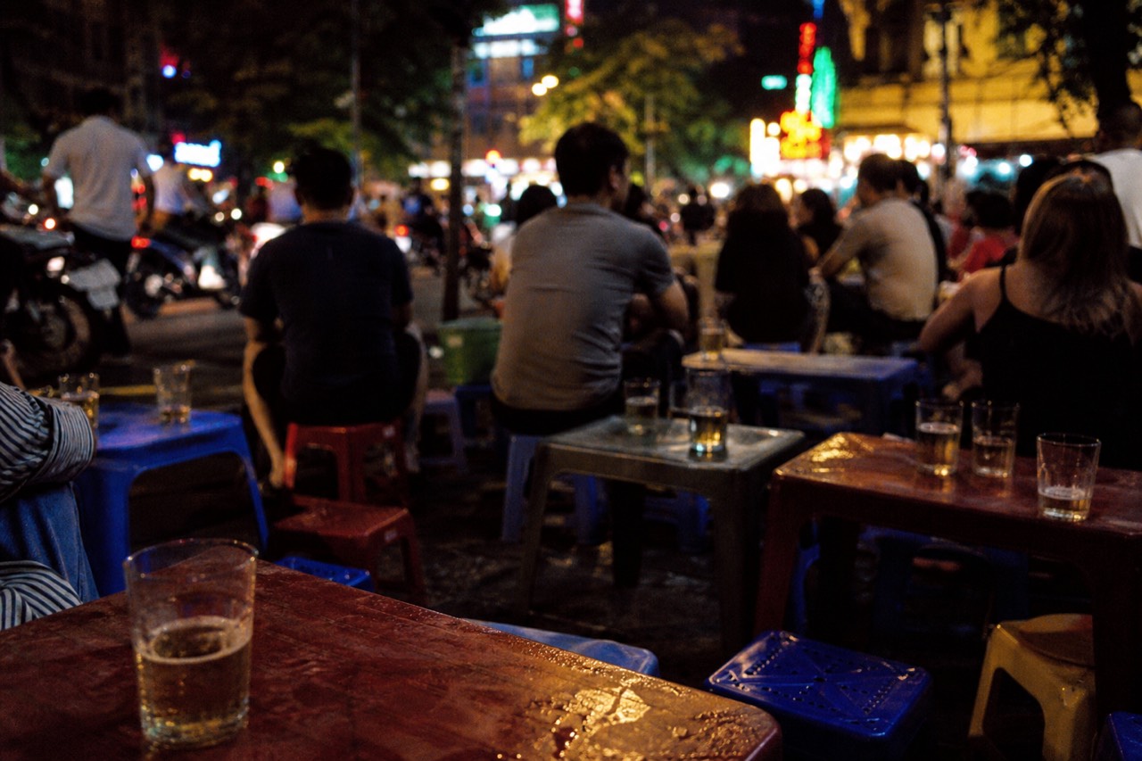 Low plastic stools and glasses of fresh bia hoi on a crowded Hanoi Old Quarter corner at night