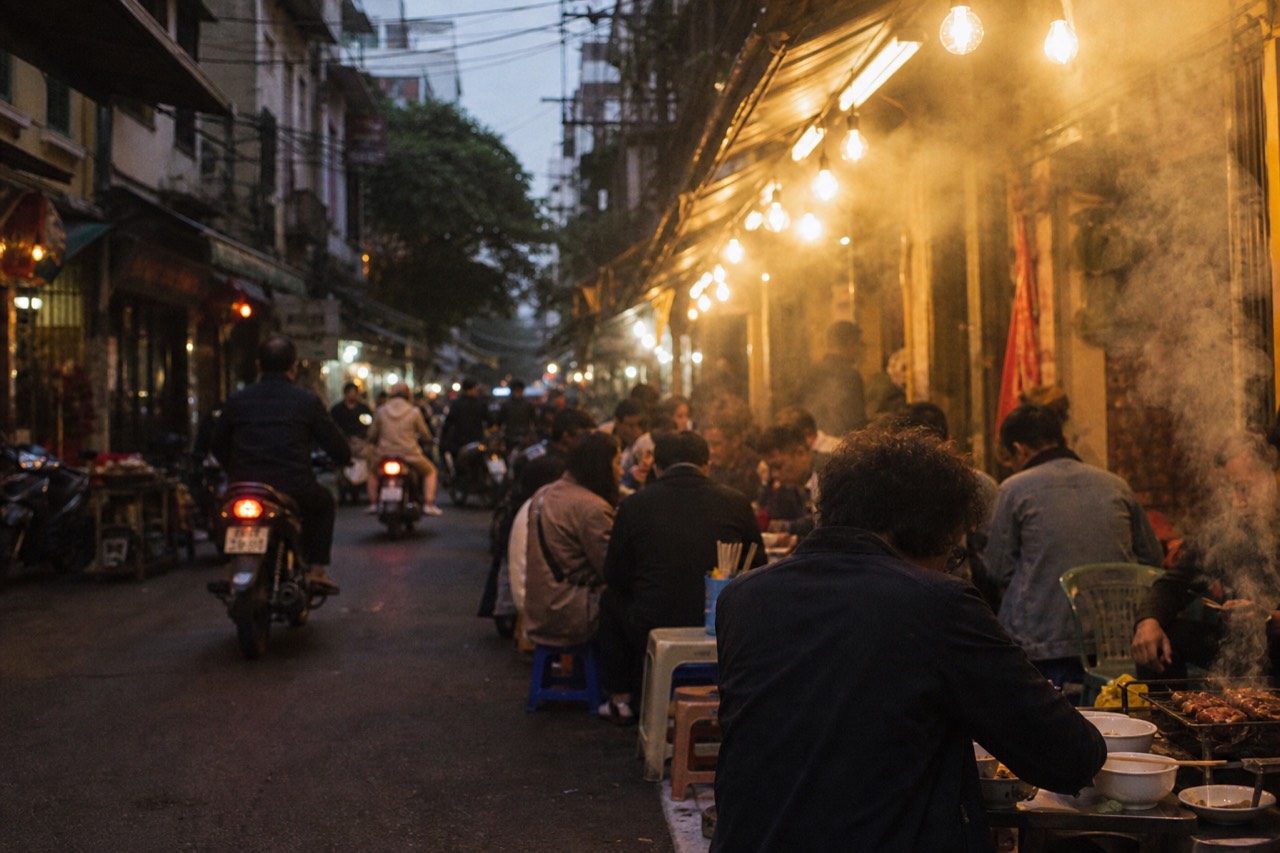 Evening crowd eating street food on low plastic stools under warm lights in Hanoi's Old Quarter