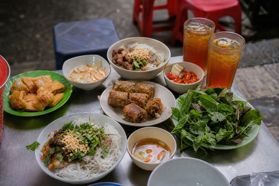 Plates of Vietnamese street food dishes shared on a small metal table in Hanoi