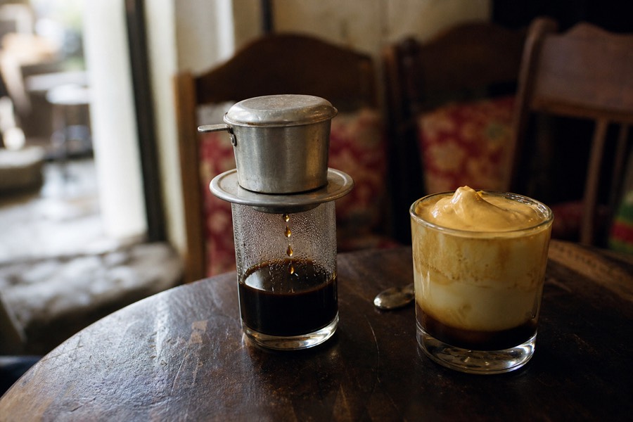 A phin filter dripping Vietnamese coffee beside a whipped egg coffee in a Hanoi cafe