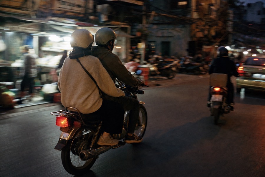A vintage motorbike weaving through Hanoi evening traffic past lit food stalls