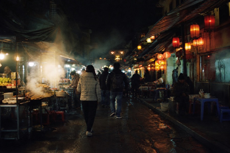 Walking tour crossing a lantern-lit Old Quarter street between food stops in Hanoi
