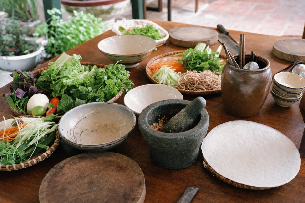 A Hanoi cooking class station with fresh market vegetables, herbs and a mortar and pestle